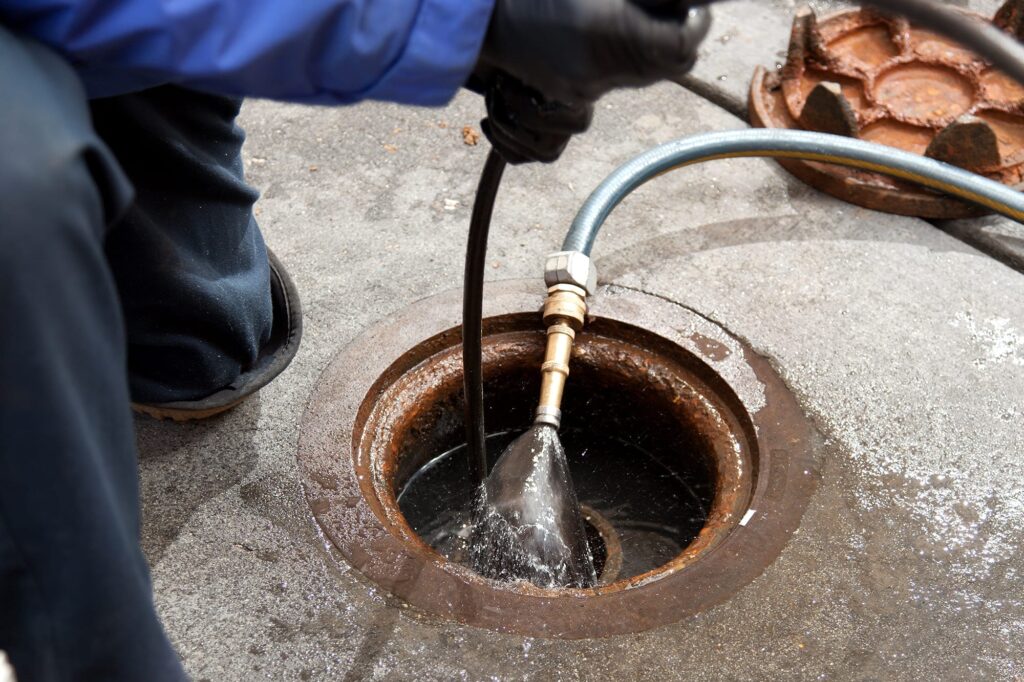Plumber hydro jetting a sewer line through a manhole in Encinitas